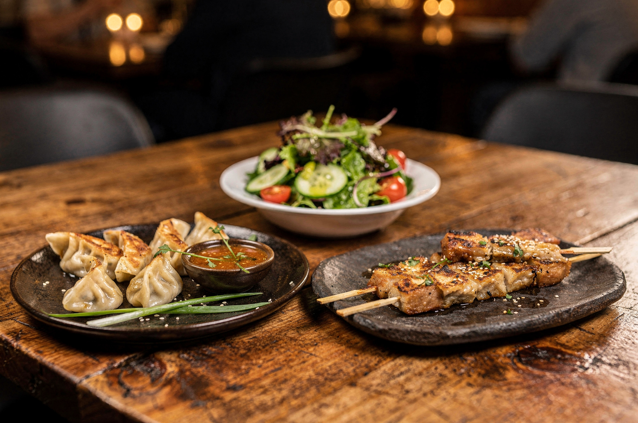 small plates of dumplings, salad, and skewers on a rustic restaurant table