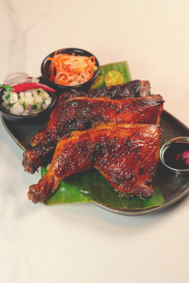 Grilled Chicken Inasal at Halina with atchara and dipping sauces on a banana leaf